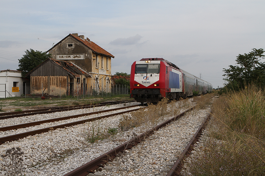 Loc 220 002 met trein uit Alexandroupoli passeert het geheel vervallen station van Polyantho (Πολύανθο), 25-09-2015<br>Let op het hekwerk met geheel links een geel bord met <i>Let op, gevaar</i>